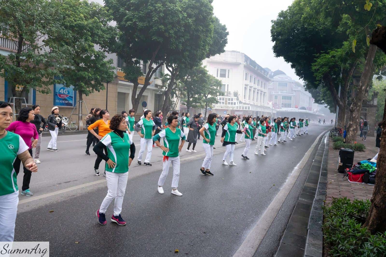 a group of people in green shirts and white pants marching down a street