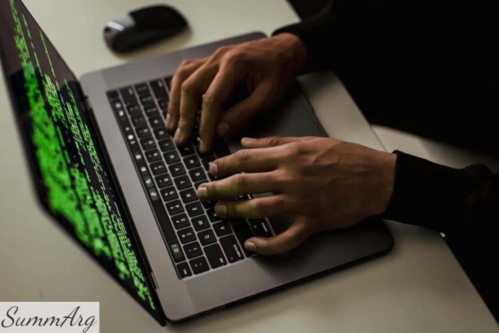 From above of crop anonymous male hacker typing on netbook with data on screen while sitting at desk