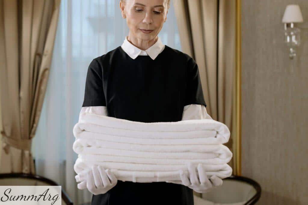 Woman in Black and White Uniform Holding a Stack of Towels